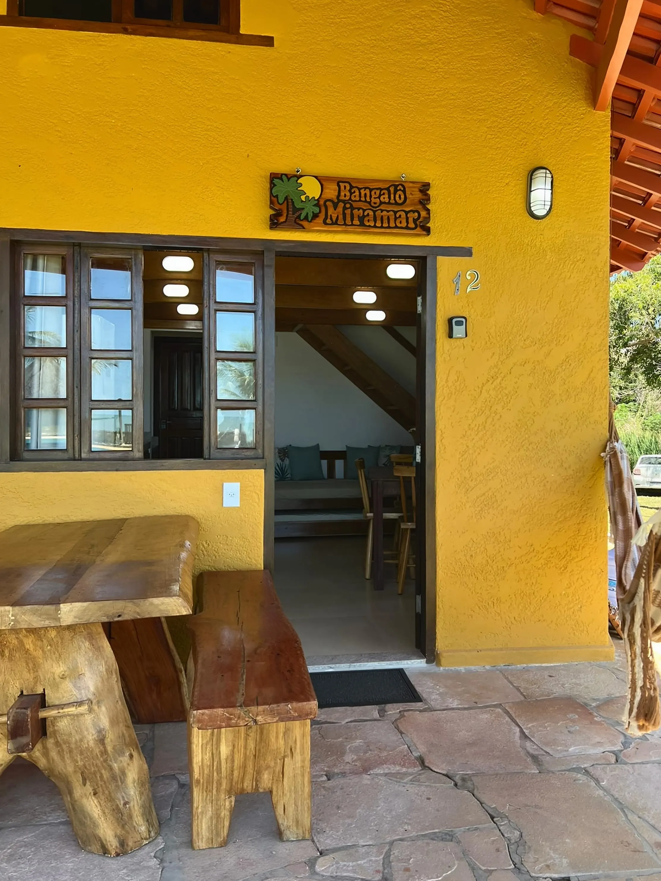 Entrada do Bangalô Miramar com a placa do bangalô, mesa e bancos de madeira