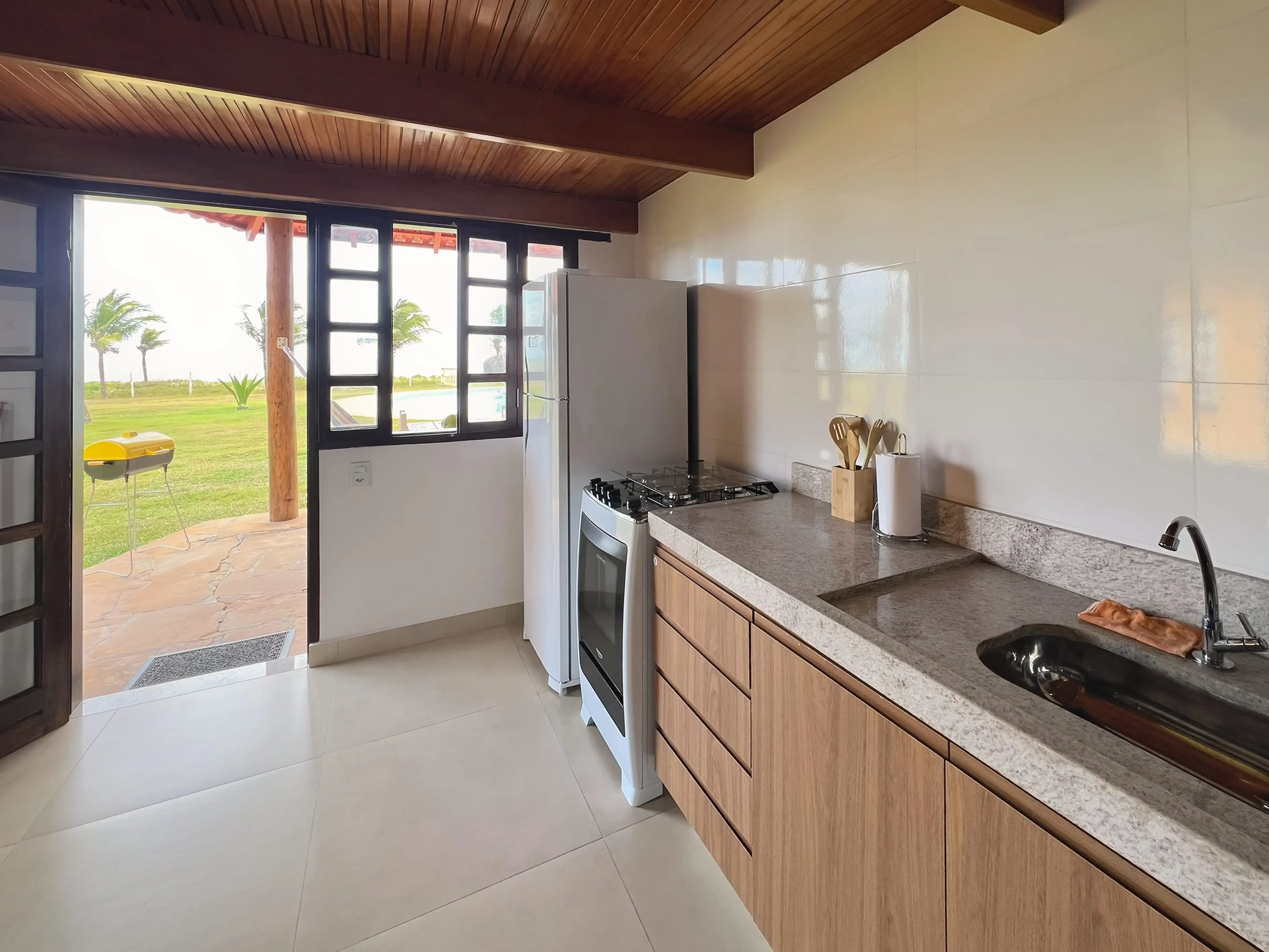 Cozinha do Bangalô Miramar com a porta aberta para o gramado e o mar ao longe